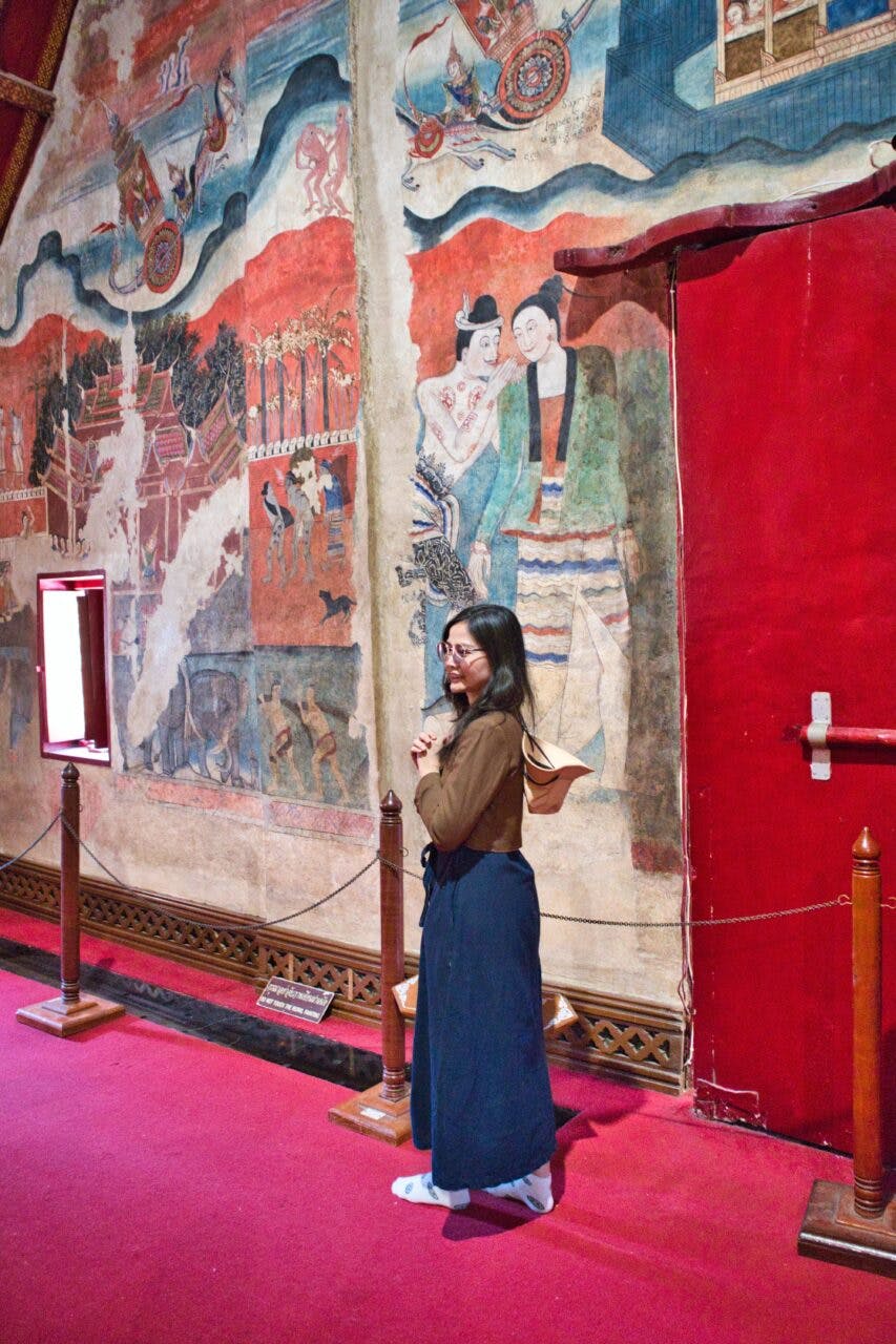 A young woman posing in front of a mural in a Thai temple, Nan, Thailand. 