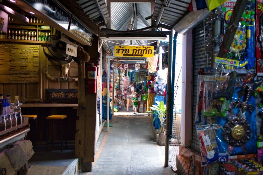 an aisle at the koh kret market with a yellow sign in Thai. In the distance you can see a tourist.